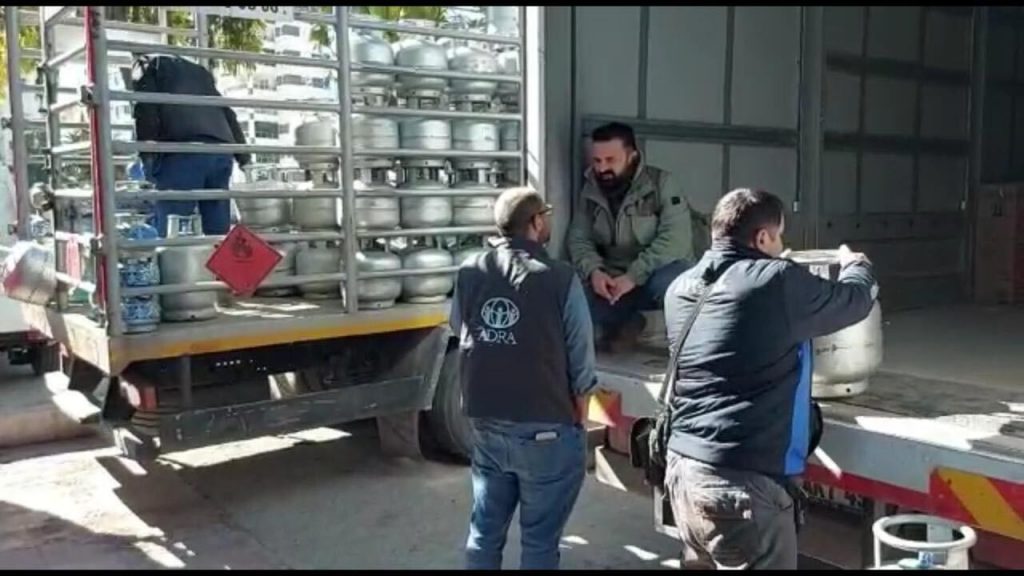 Three men unload a truck with gas heaters. One is wearing the ADRA logo