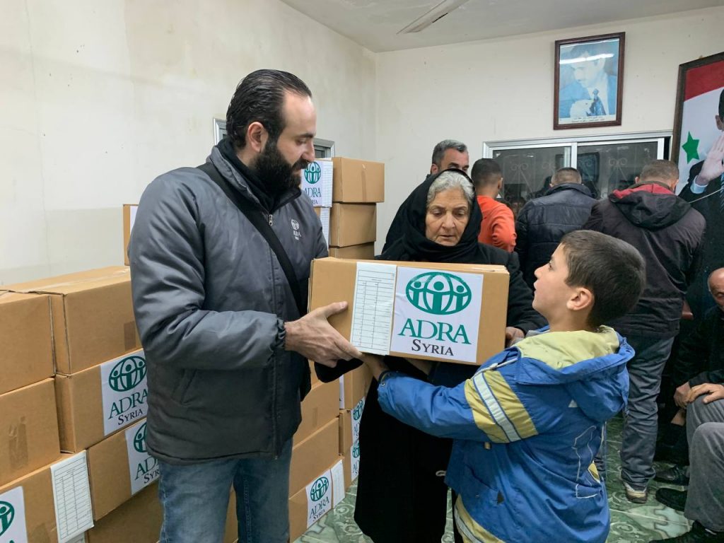 An ADRA staff member hands over a food parcel to a young boy