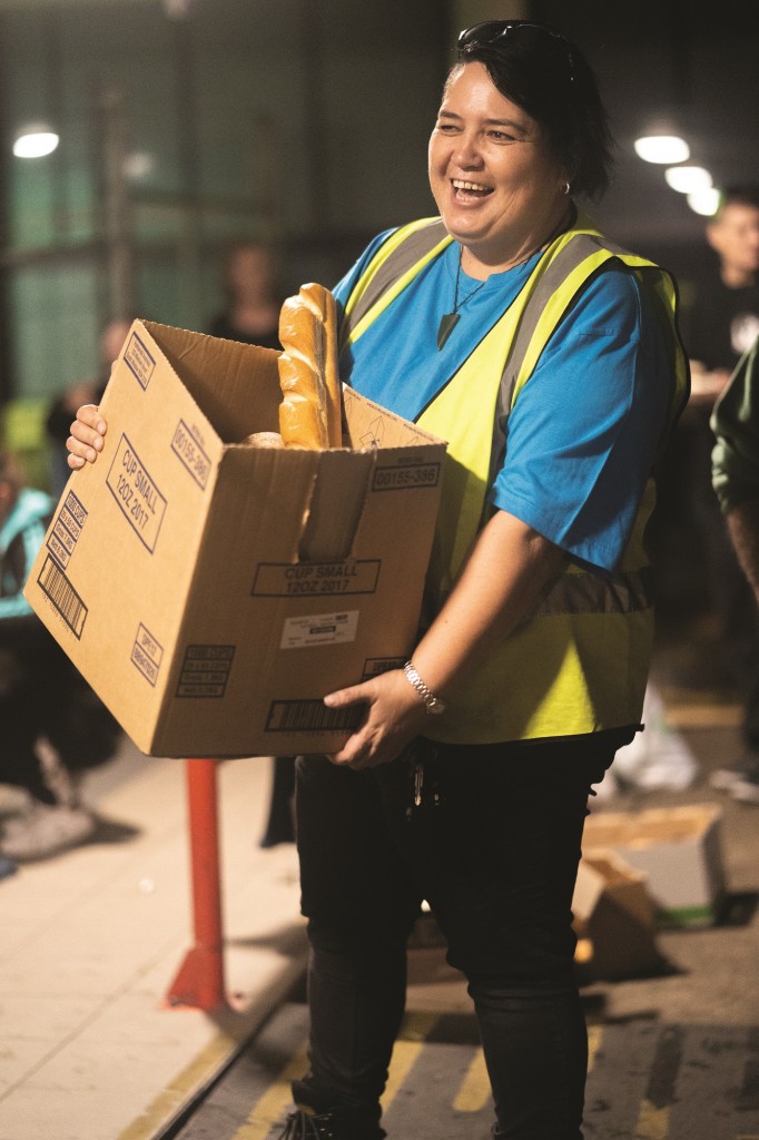 Lady in fluro vest carrying a box of bread