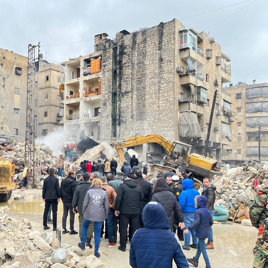 ADRA's Turkey Response. Collapsed building with first responders digging through rubble, including a woman in an ADRA vest.